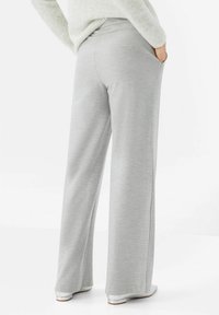 Pantalon gris clair à jambes larges en tissu doux, avec une ceinture lisse et des poches latérales, conçu pour le confort et la liberté de mouvement.