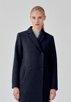 Manteau en laine bleu marine avec design croisé, col cranté, poches latérales et deux boutons noirs. Texture lisse et coupe ajustée.