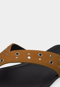 Μαύρο σανδάλι με φαρδιά καφέ λουράκι διακοσμημένο με ασημένιες και λευκές κυκλικές τρουκς μπροστά.