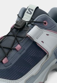 Πολύχρωμο αθλητικό παπούτσι με γκρι και ναυτικό μπλε επάνω μέρος, λεπτομέρειες από δίχτυ, ελαστικό σύστημα κορδονιών και χαρακτηριστική μολυβδούχα εξωτερική σόλα.