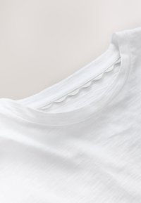 Biele bavlnené tričko s okrúhlym výstrihom a oblými prešívaniami na golieri, s jemnou, hladkou textúrou.