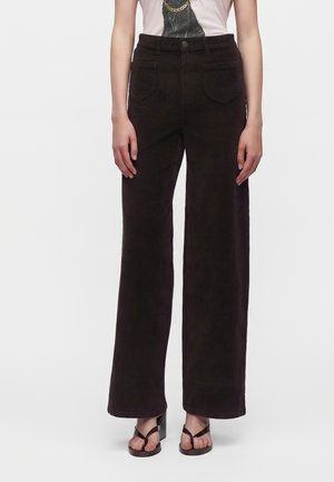 Femme portant un pantalon en velours côtelé noir taille haute à jambes larges avec poches avant et des sandales noires à talons avec brides à la cheville.
