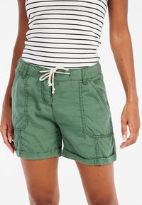 Groene katoenen short met een trekkoord in de taille, zijzakken en omgeslagen zomen. De stof heeft een soepele textuur met zichtbare stikdetails.