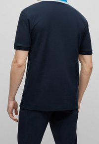 Marinblå piké med kort ärm, en vit och ljusblå krage, sidslitsar vid nederkanten och mjuk bomullsstruktur.