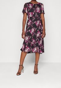 Flödande svart klänning med abstrakt mönster i lila och vitt, korta fjärilsärmar, wrap-design, åtsittande midja och utsvängd kjol.