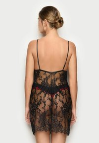 Negligee in pizzo nero con spalline sottili, caratterizzato da un motivo floreale, orlo scallop e un accento rosso a contrasto in vita. Tessuto trasparente.