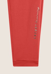 Leggings deportivos rojos con un diseño ajustado, hechos de una tela elástica. Presentan un texto de logo plateado a lo largo del costado y puños acanalados.