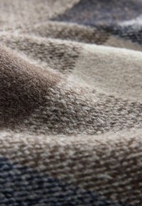 Gros plan d’un tissu doux et texturé avec une surface ondulée dans des nuances de beige et de marron.
