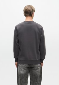 Szara bluza z okrągłym dekoltem, ściągaczami przy mankietach i u dołu. Miękka tekstura, prosta konstrukcja bez widocznych logo czy wzorów.