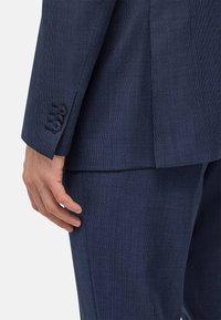 Veste de costume bleu marine texturée avec trois boutons aux poignets, affichant une coupe ajustée et des lignes épurées à l'ourlet et au col.