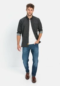 Mørkt mønstret skjorte med krave, op-rullede ærmer, parret med blå jeans og brune lædersko. Enkel, afslappet påklædning.