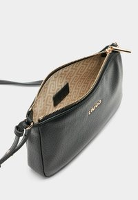 Borsa a mano nera in pelle con una superficie texturizzata, hardware in tonalità oro e un interno beige con motivo, dotata di chiusura con zip e tracolla regolabile.