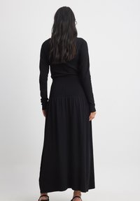 Long black dress with a fitted top and flared bottom, featuring long sleeves and a gathered waist, made from soft fabric.