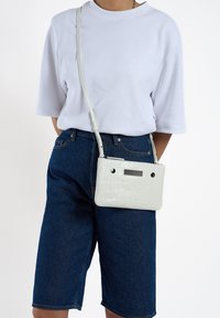 Kruipdiep grijze schoudertas met krokodillenpatroon, met een gladde textuur, eenvoudig ontwerp, twee zwarte accenten en een lange schouderband.