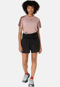 Light pink textured athletic shirt with brown accents, paired with black shorts and multicolored running shoes. Waistband holds a water bottle.