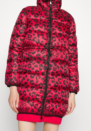 Doudoune rouge et noire imprimé léopard avec fermeture éclair devant et logos « Love Moschino » portée sur une jupe rouge.
