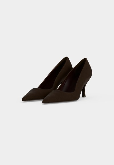 Paire de chaussures à talons hauts brun foncé avec des bouts pointus sur un fond clair uni.