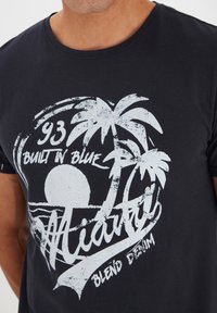 Crna pamučna majica s bijelim grafičkim dizajnom koji prikazuje palme, sunce i natpis "Miami", sa efektom istrošenosti.