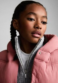 Jachetă pufosită roz cu guler înalt, strat interior gri cu fermoar și un tricou alb dedesubt. Textură fină cu accente metalice.