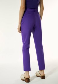 Lila skräddarsydda byxor med smal passform, bälteshällor och bakfickor. Bärs med ljusa träskor som har klack av trä.