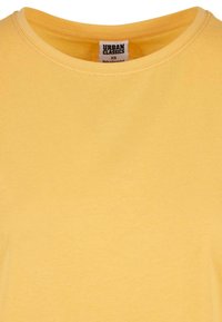 T-shirt jaune à col rond avec étiquette de la marque Urban Classics visible indiquant la taille XS et fabriqué au Bangladesh.