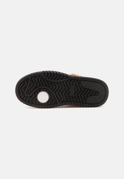 Semelle de chaussure en caoutchouc noir avec un motif en zigzag et un élément circulaire blanc près du talon, sur un fond blanc uni.