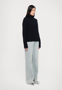 Marineblauer Strickrollkragenpullover mit Zopfmuster, lockerer Schnitt und langen Ärmeln, kombiniert mit hochgeschnittenen, hellblauen weit geschnittenen Jeans.