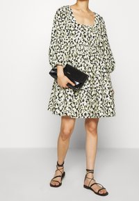 Šaty s květinovým vzorem, čtvercovým výstřihem, nabíranými rukávy, staženým pasem a rozšířenou sukní. Kombinováno s černým psaníčkem a plochými sandály.