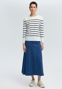 Sweter z długim rękawem w paski w kolorze kremowym i granatowym, połączony z niebieską spódnicą maxi z denimu z przednimi szwami oraz trampkami.