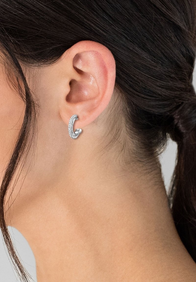 Boucles d'oreilles en argent avec une finition polie, présentant un bord texturé et un subtil éclat provenant de petites pierres incrustées.