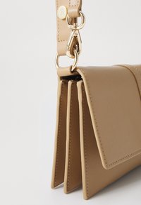 Brązowa skórzana torba o strukturalnym kształcie, z trzema przegródkami, złotymi elementami metalowymi oraz odpinanym paskiem dla większej wszechstronności.