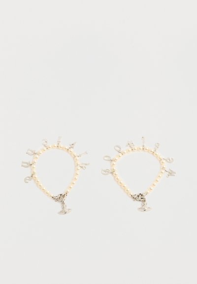 Δύο βραχιόλια από πέρλες με ασημένια μοτίφ γράμματα και ένα στρογγυλό ασημένιο μενταγιόν σε λευκό φόντο.