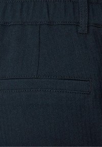 Dark blue herringbone-patterned fabric with a smooth texture. Features a back pocket with narrow flap and straight stitching detail.