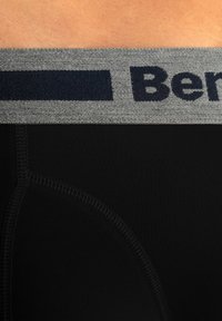 Mutande nere con un elastico grigio in vita e testo blu marino. Texture liscia, design aderente e dettagli di cucitura rinforzati.