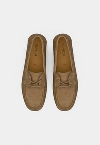 Καφέ μοκασίνια από σουέντ με στρογγυλεμένη μύτη, δέσιμο με κορδόνια και χρυσαφί οπές. Λογότυπο και μέγεθος τυπωμένα στην πάτημα. Επίπεδη σόλα.