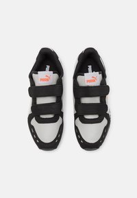 Un par de zapatillas Puma en blanco y negro con logo naranja, que cuentan con dos correas de velcro negras sobre un fondo blanco.