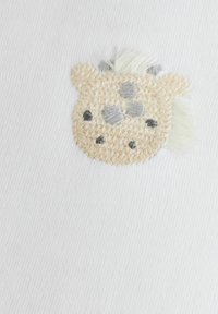 Weißer Stoff mit einem gestickten Giraffenkopf in Beige, Grau und Schwarz, mit strukturierten Details und einem Büschel weicher weißer Haare.