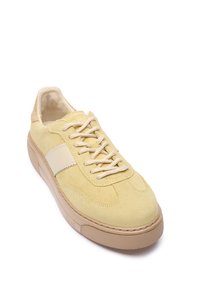 Żółty zamszowy sneaker z kremowym skórzanym paskiem, okrągłym noskiem i fakturowaną gumową podeszwą. Wyposażony w beżowe sznurówki i wyściełany język.
