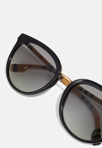Óculos de sol oversized pretos com lentes degradê e uma ponte dourada, apresentando braços de tartaruga texturizados com acentos em vermelho e azul.