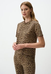 Korte mouwen, bruin shirt met luipaardprint van zachte stof. Heeft een ronde halslijn en een ontspannen pasvorm, gecombineerd met bijpassende, gestreepte broeken.