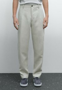 Pantaloni beige chiaro realizzati in tessuto liscio, con un design a gamba dritta, tasche frontali e chiusura a un bottone.