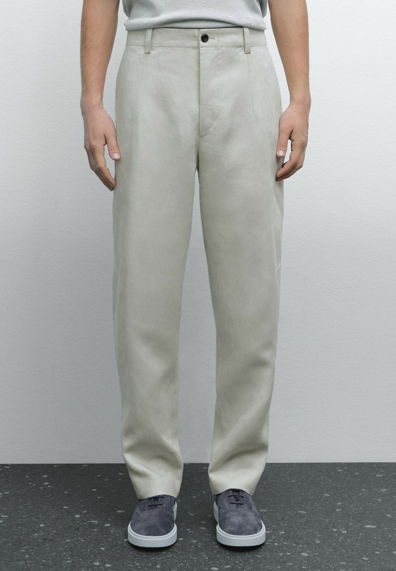 Pantaloni beige chiaro realizzati in tessuto liscio, con un design a gamba dritta, tasche frontali e chiusura a un bottone.
