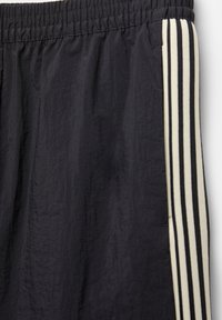 Shorts atletici negri dintr-un material ușor, cu o suprafață texturată, talie elastică și accente verticale în dungi crem și negre.