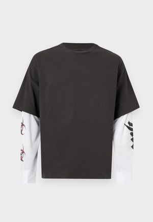 Μαύρο κοντομάνικο μπλουζάκι φορεμένο πάνω από λευκό μακρυμάνικο πουκάμισο με κόκκινα και μαύρα αφηρημένα σχέδια στα μανίκια.