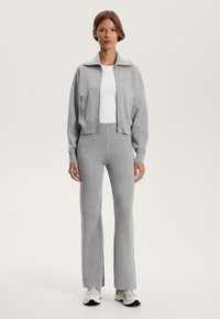 Siva pletena skrajšana jakna z zadrgo spredaj, v kombinaciji z usklajenimi visokimi širokimi hlačami. Obe kosu imata mehak teksturo.