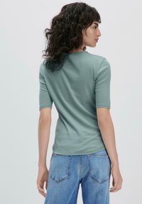 Lyhythihainen, istuva t-paita pehmeästä mintunvihreästä kankaasta, jossa on pyöreä kaula-aukko, yhdistettynä vaaleansinisiin farkkuihin, joissa on takataskut.