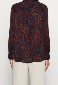 Mörk paisleyblus med lång ärm, prydd med röda, blå och gyllene mönster. Taperad passform med knapplist och en ryggsömnadsdetalj.