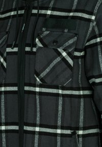 Schwarz-grau kariertes Jacke mit durchgehendem Reißverschluss, zwei Brusttaschen und einer strukturierten Stofftextur. Das Etikett befindet sich auf der linken Schulter.