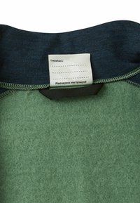 Grüner Fleece-Stoff mit einem dunkelblauen Kragen. Das Etikett zeigt einen leeren Bereich mit dem Text "Ich war hier: Bitte pass mich weiter!" auf weißem Hintergrund.