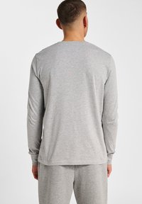 Jasnoszara koszula z długim rękawem, z okrągłym dekoltem i prążkowanymi mankietami, wykonana z miękkiego, strukturalnego materiału. Noszona z pasującymi spodniami.